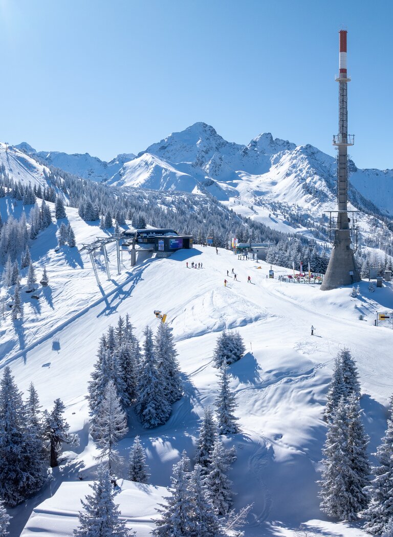 Snowy ski area with transmission tower, lift station and mountains under blue sky | © Hauser Kaibling Seilbahn- und Liftges.m.b.H. & Co KG