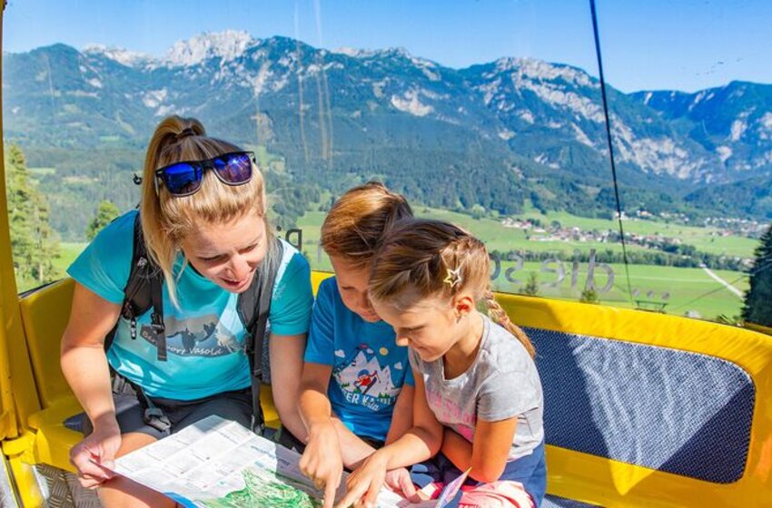 Familienausflug mit Panoramablick in der Sommergondel | © Hauser Kaibling Seilbahn- und Liftges.m.b.H. & Co KG Eine Mutter und zwei Kinder betrachten eine Wanderkarte in einer gelben Gondel mit Blick auf grüne Täler und Berglandschaft im Sommer. | © Hauser Kaibling Seilbahn- und Liftges.m.b.H. & Co KG