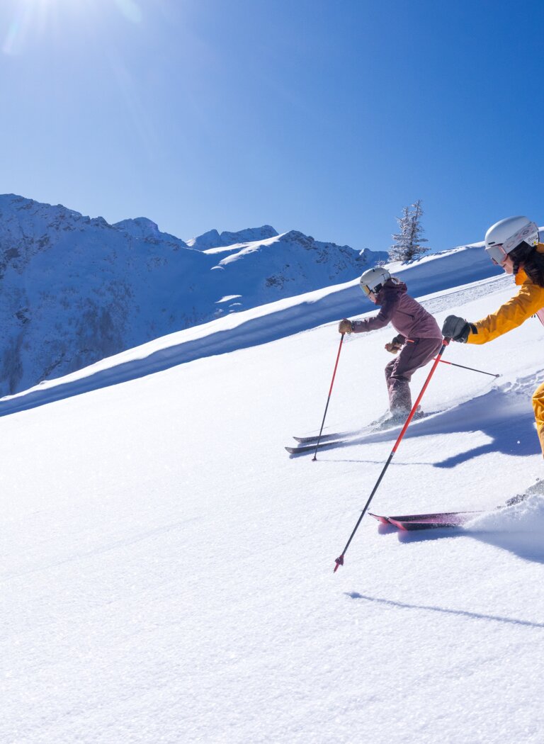 Two female skiers ride through fresh powder snow on a sunny slope in the Alps | © Hauser Kaibling Seilbahn- und Liftges.m.b.H. & Co KG