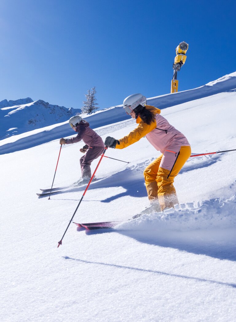 Zwei Skifahrerinnen fahren bei Sonnenschein durch frischen Tiefschnee auf einem Alpenhang | © Hauser Kaibling Seilbahn- und Liftges.m.b.H. & Co KG
